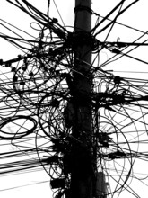 A power pole with a messy tangle of cables in an urban environment, black and white, Prizren,