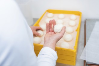 Baker presents dough ball in hand in front of a yellow box full of dough balls, bake rolls,