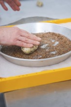 Hands press dough into seeds within a round pan to prepare, bake rolls, Haselstaller Hof,