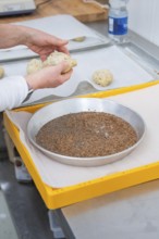 Person molding dough pieces with hands on a yellow tray in a kitchen, baking rolls, Haselstaller