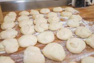 Many pieces of dough on a floured wooden board, ready for further preparation, bake rolls,