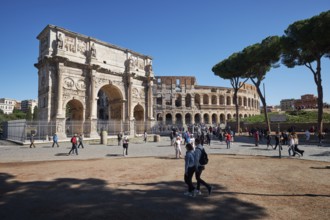 Arch of Constantine and Colosseum surrounded by tourists under blue sky and green grass, Rome,