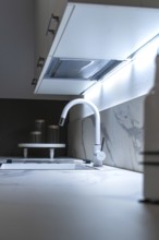 Minimalist kitchen corner with white worktop and illuminated back wall