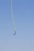 Female bungee jumper in midair with her ankles tied to a long yellow elastic bungee jumping cord,