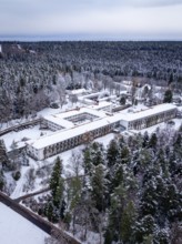 Aerial view of a snowy forest with a complex of buildings surrounded by pine trees, rehab clinic,