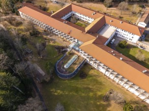 A building complex with a red roof and a spacious courtyard with green space from a bird's eye