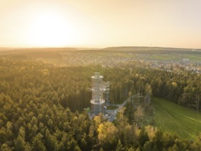 A tower towers over a forest, the view extends to a city in warm sunset light, Himmelsglück