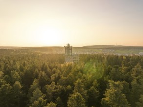 An observation tower rises above a green forest under a golden sunset, Himmelsglück observation