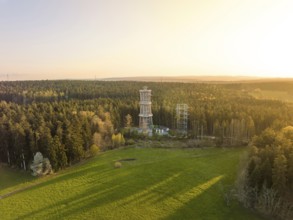 A tower stands in the middle of a forest next to a meadow, illuminated by warm sunlight,