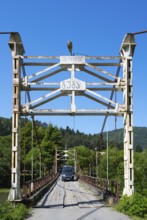 Car drives over an old suspension bridge surrounded by forest, camper, motorhome on a suspension