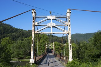 Steel bridge crosses a river amidst forested mountains, suspension bridge across the Kura River