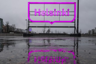 Large pink glowing city logo of Helsinki, in front of Oodi Central Library and Cultural Center,