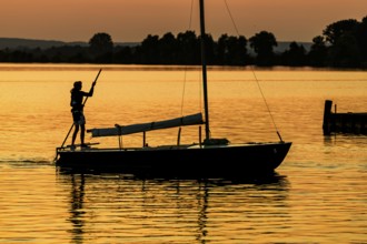 Sailing boat with person on calm Dümmer See brought into the harbor with a long stake at sunset,