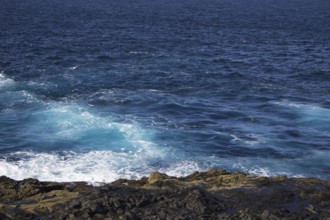 Waves break on a rocky coastline under deep blue skies, Yaiza Lanzarote