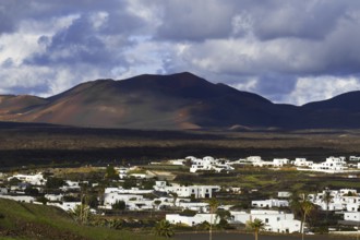 Partial view of the municipality of Yaiza at the foot of volcanic mountains under dramatic clouds