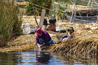 Woman and child work in a rural scene on the shores of a lake surrounded by reeds, The floating