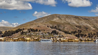 View of a lakeside village with hills in the background and clouds in the sky, The floating reed