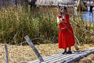 Woman in traditional dress rides a wooden reed boat in a lake, The floating reed islands of Uros in