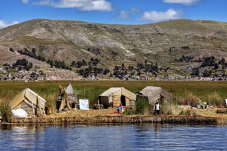 Huts on a reed island in front of a village and mountains, reflecting in the water, The floating