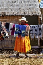 Woman showing colorful, handmade cloths in front of a thatched hut, The floating reed islands of