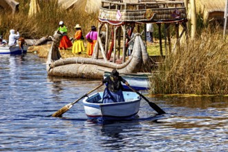A woman rows in a waterway between large reed canoes and village life, The floating reed islands of