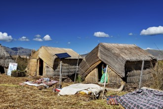 Several reed huts with solar panels under a blue lakeside sky, The floating reed islands of the