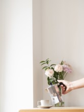 Woman is pouring coffee from moka pot into cup on wooden table with flowers in vase