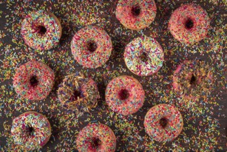 Donuts with sprinkles on wooden table, colorful ornaments scattered