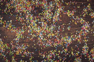 Colourful sprinkles scattered on dark wooden table
