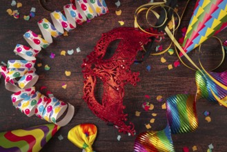 Red mask surrounded by party decorations such as streamers and confetti on table, carnival