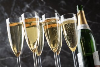 Six glasses filled with sparkling wine and an open champagne bottle against a black background