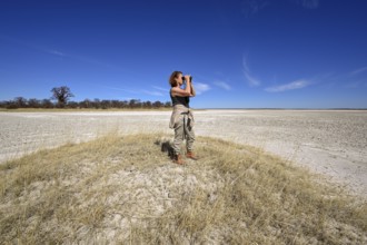 Tourist observes animals through binoculars near the Baines Baobabs, Kudiakam Pan, Nxai-Pan