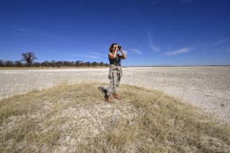 Tourist observes animals through binoculars near the Baines Baobabs, Nxai-Pan National Park, near