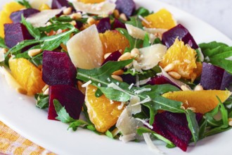 A salad made with chunks of beet, orange slices, and arugula. It is topped with cheese shavings and