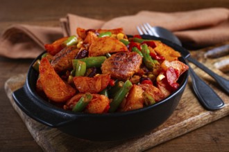 Steakhouse pfanne, fried potato slices, with meatballs, and vegetable mixture, on a black plate