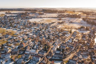 Aerial view of a snowy village with adjacent fields in the soft light of a winter sunset,