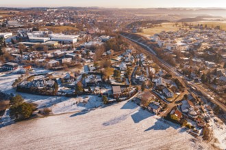 Aerial view of a rural village, partly covered by snow, with roads and trees under clear sky,