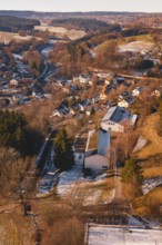 Small settlement with snow-covered houses and roads, surrounded by forest landscape, Aach,