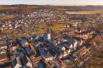 Aerial view of a town with church and buildings in evening light, surrounded by hills and fields,