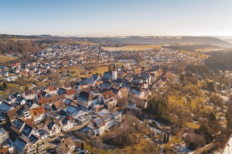 Aerial view of a town with a central church surrounded by red roofs and winter landscape under blue