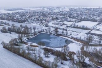 Snowy village panorama with central lake and surrounding fields from the air, Empfingen,