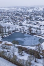 Snowy village with frozen lake seen from above on a grey day, Empfingen, Freudenstadt district,