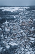 A snow-covered city from the air with many houses and a river, surrounded by hills and forests in a