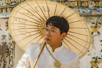 Young man wearing a parasol in traditional clothing presents himself for the photographers, Wat