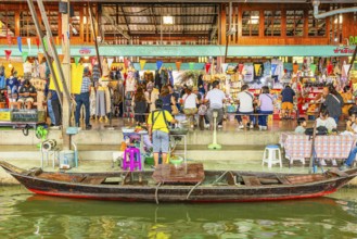 Wooden boat on the Damneon Saduak floating markets channel, behind shops and restaurant, near