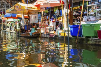 Wooden boat and umbrellas are reflected on the Damneon Saduak floating market channel near Bangkok,