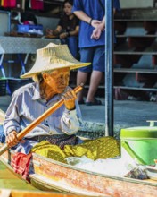 Old woman with her wooden boat on the Damneon Saduak floating markets channel, near Bangkok,