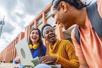 Three young, diverse students are happily laughing and sharing a lighthearted moment while