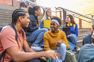 Diverse group of young students sitting on university campus steps, happy and smiling while