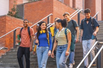 Diverse group of smiling university students walking down outdoor stairs on campus together,